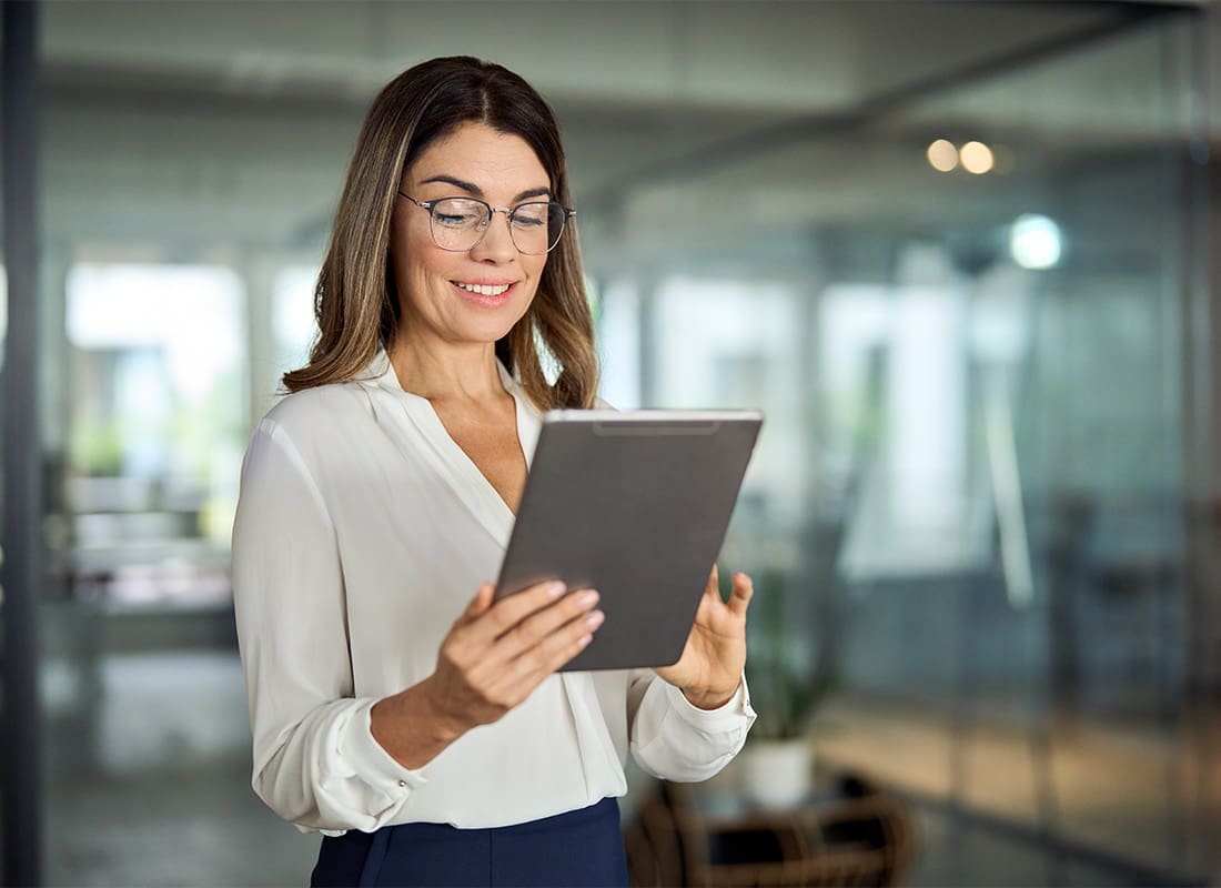 Report a Claim - Middle Aged Business Woman Standing in a Small Office While Using a Tablet